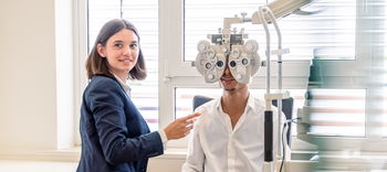 Das Bild zeigt eine Mitarbeiterin, die einen Sehtest mit einem Kunden macht.