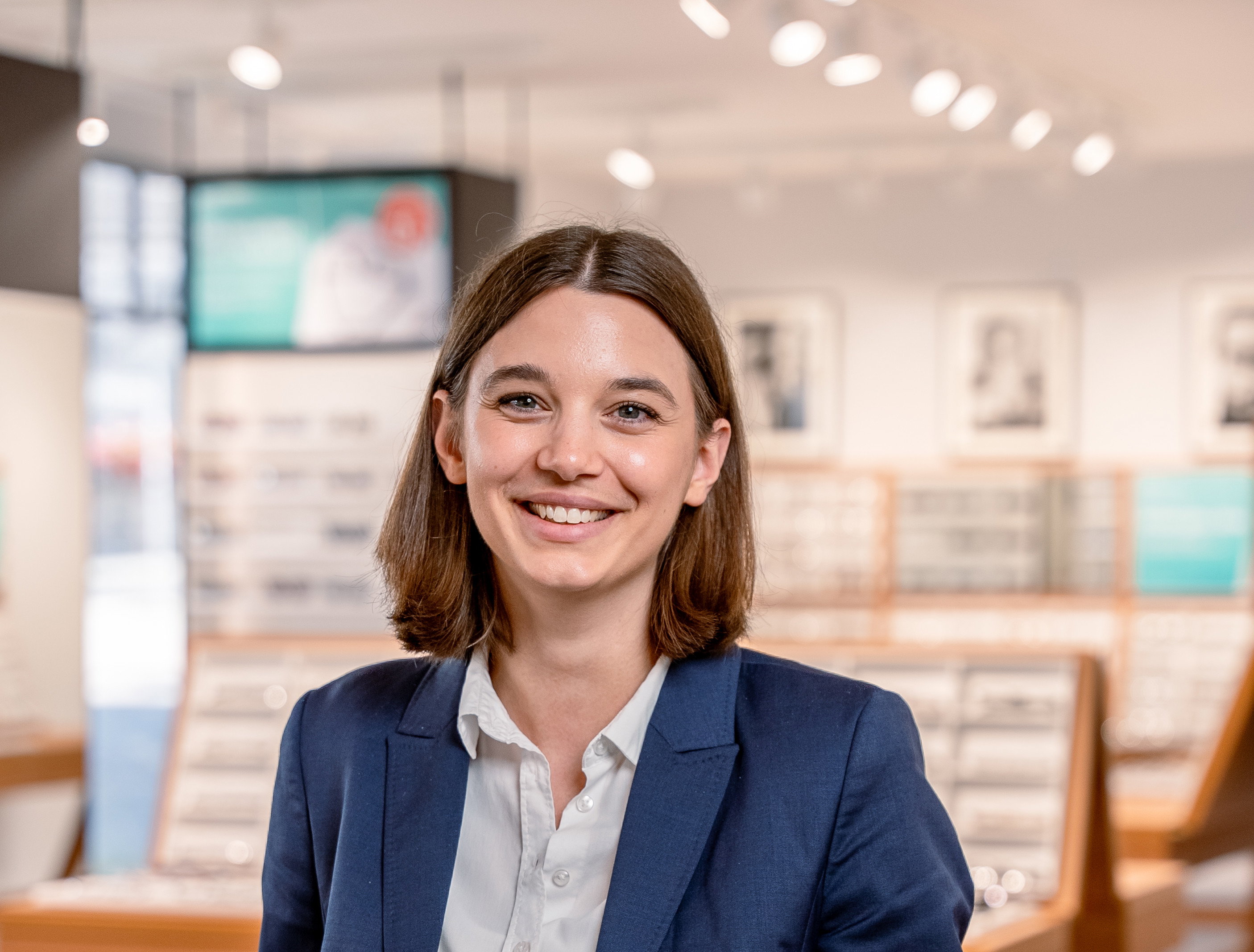 Das Bild zeigt eine fröhliche junge Frau in einem blauen Blazer.