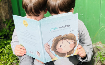 Das Bild zeigt zwei kleine Jungs, die in der Natur sitzen und unser Kinderbuch lesen.