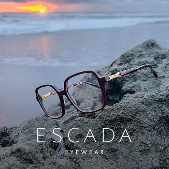Zu sehen ist eine Brille von Escada auf einem Stein am Strand mit Sonnenuntergang im Hintergrund.