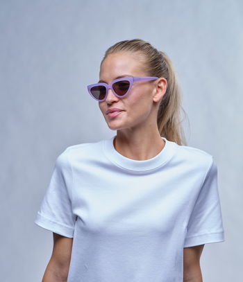 Das Bild zeigt eine Frau mit einer Sonnenbrille in Lila