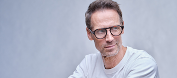 Das Bild zeigt einen Mann mit weißem T-Shirt und einer braunen Kunststoffbrille.