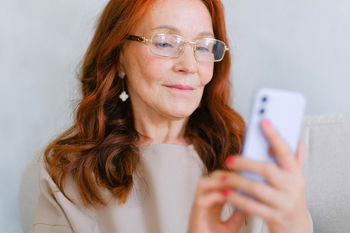 Das Bild zeigt eine rothaarige Frau mit Brille, die auf ein Smartphone schaut.