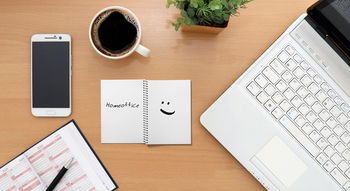 Zu sehen ist ein Schreibtisch mit Laptop, IPhone, Kalender, Block und Tasse.