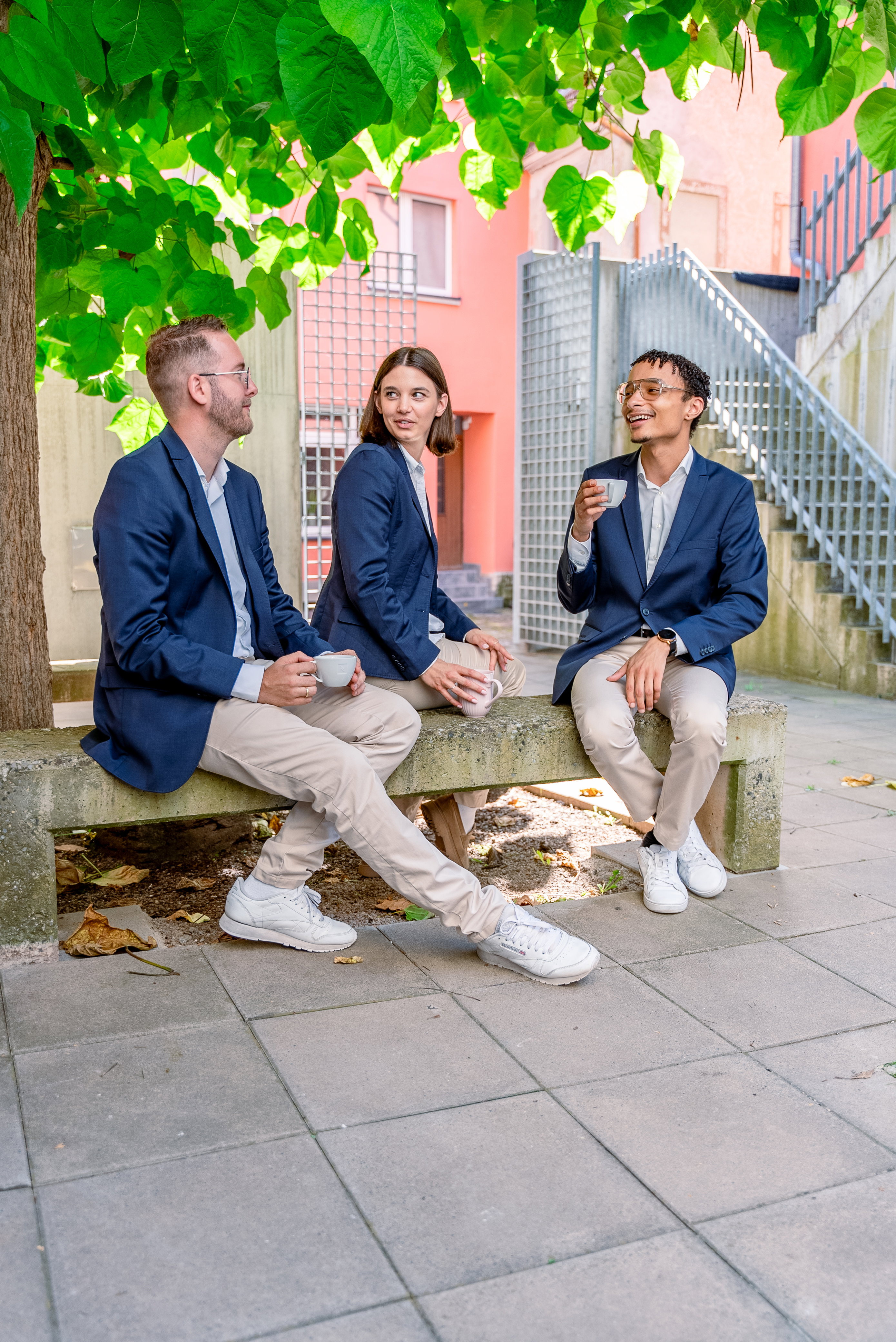 Das Bild zeigt drei Mitarbeiter, die unter einem Baum sitzen und eine Kaffeepause machen.