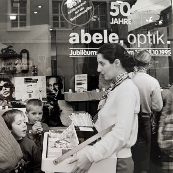 Das Bild zeigt eine Frau mit Bauchladen und Kunden bei unserer 50-Jahr Feier.