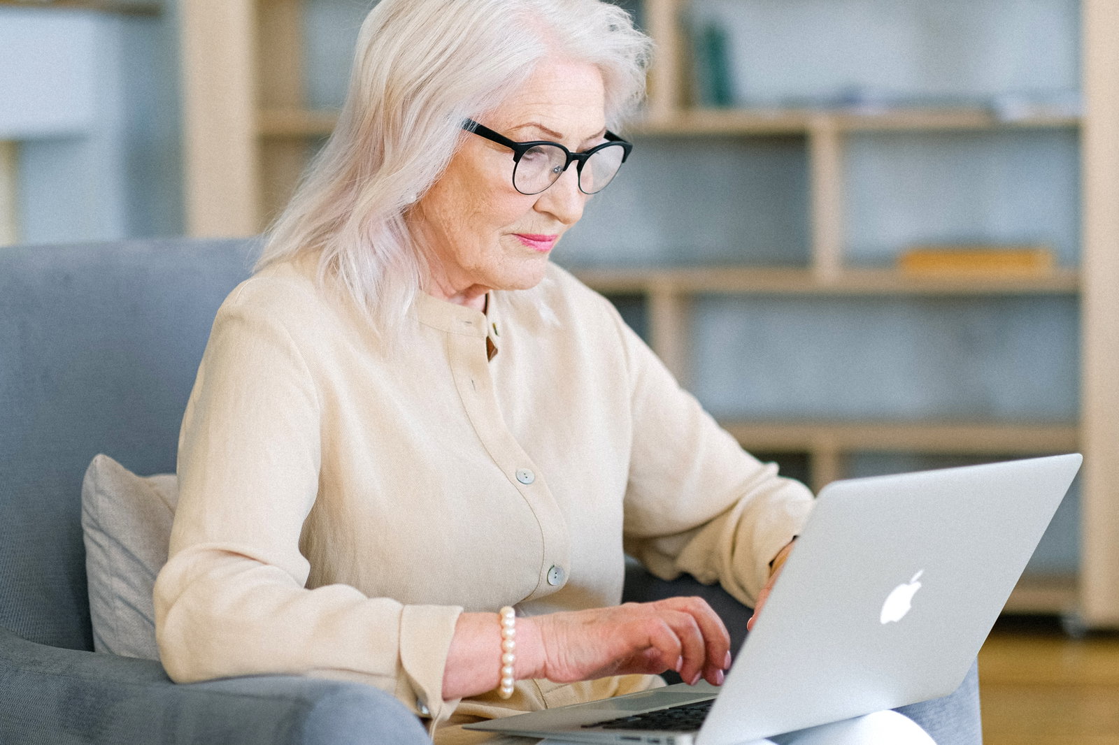 Das Bild zeigt eine ältere Dame mit Brille, die vor einem Laptop sitzt.