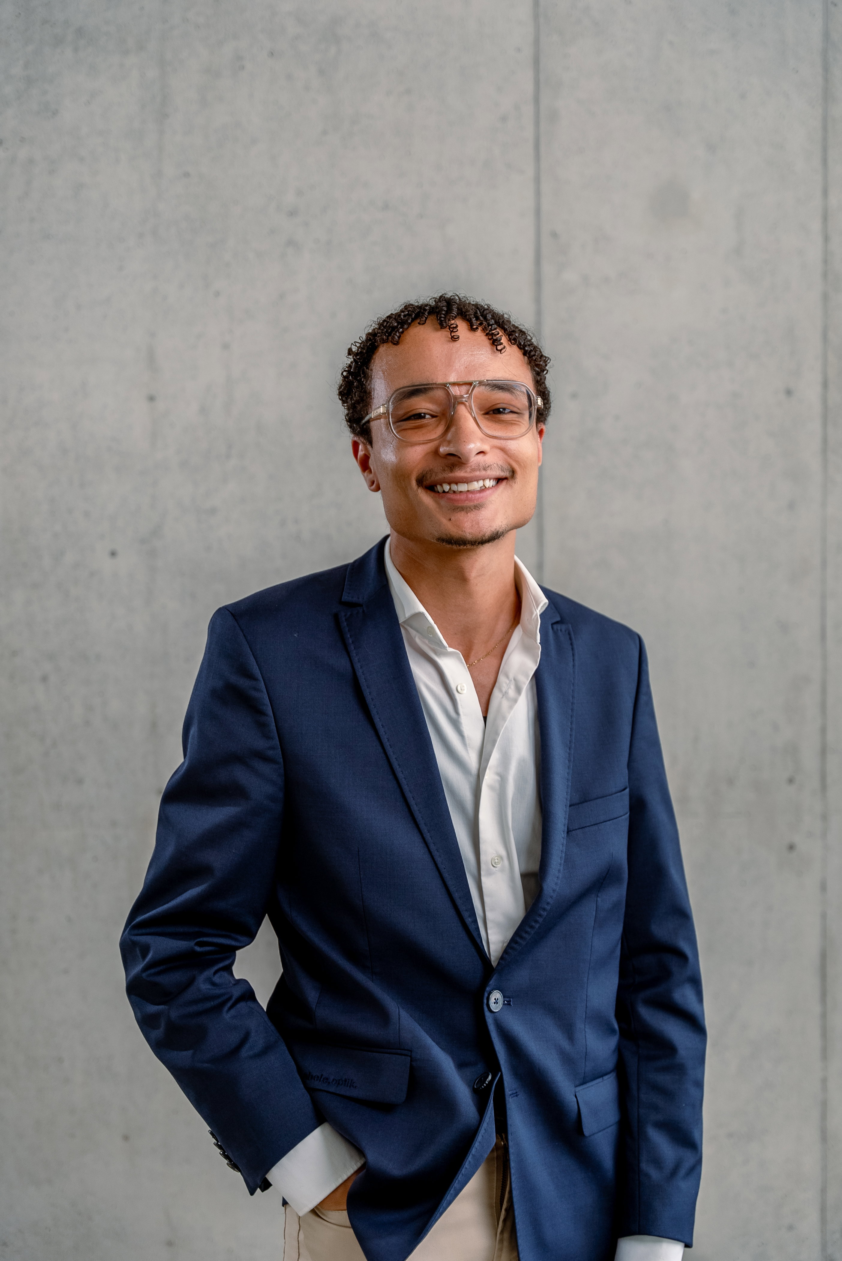 Das Bild zeigt einen jungen Mann mit Brille in blauem Sakko.
