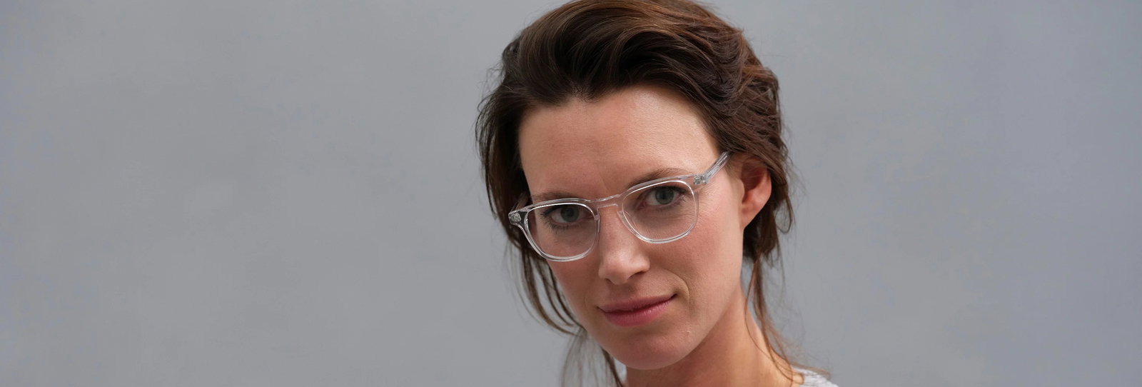 Das Bild zeigt das Gesicht einer Frau mit Brille vor grauem Hintergrund.