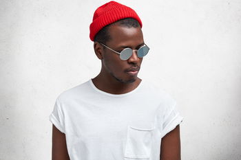 das Bild zeigt einen jungen Mann im weißen T-Shirt und roter Mütze mit verspiegelter Sonnenbrille
