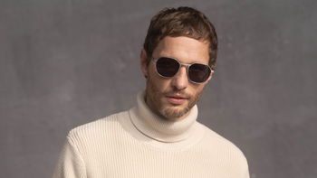 Das Bild zeigt einen Mann mit Sonnenbrille in einem beigen Rollkragenpullover.