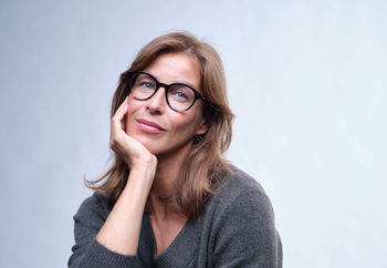 Eine Frau mit Brille und grauem Pullover stützt ihr Kinn auf ihrer Hand ab.