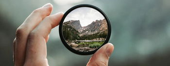 Das Bild zeigt eine Berglandschaft, die durch ein Lupenglas betrachtet wird.