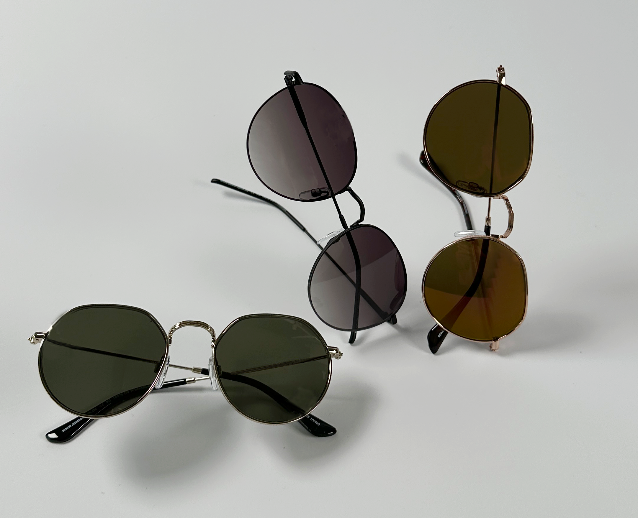 zu sehen sind drei Abele Optik Sonnenbrillen mit bunt getönten Gläsern (grün, braun, violett) vor weißem Hintergrund