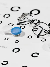 Zu sehen ist eine Sehtest-Tafel, eine Brille und ein Kontaktlinsen Aufbewahrungsbehälter