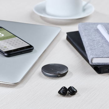 Das Bild zeigt Hörgeräte auf einem Schreibtisch liegend. Daneben sind ein Laptop, ein Handy, ein Notizbuch und eine Kaffeetasse zu sehen.