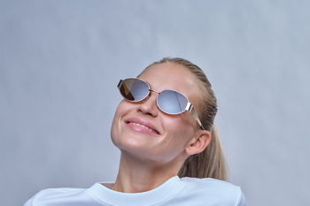 Zu sehen ist eine glückliche junge Frau mit verspiegelter ovaler Sonnenbrille.