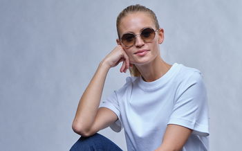Das Bild zeigt eine Frau mit Pferdeschwanz und weißem T-Shirt und Sonnenbrille.