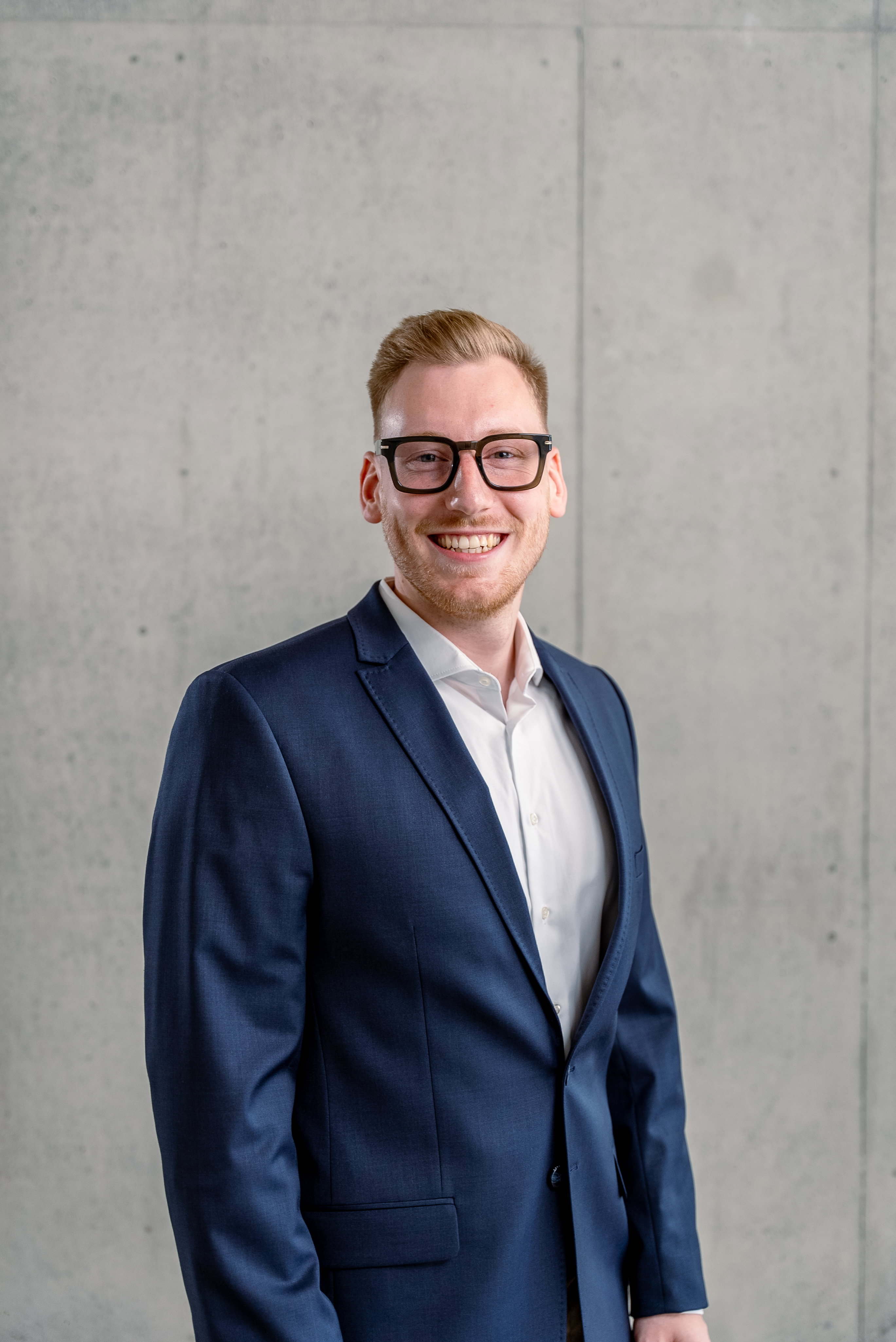 Das Bild zeigt einen Mann im Sakko vor einer Betonwand.