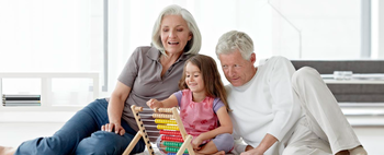 Das Bild zeigt eine ältere Frau und einen älteren Mann, die mit ihrer Enkelin auf dem Teppich spielen.